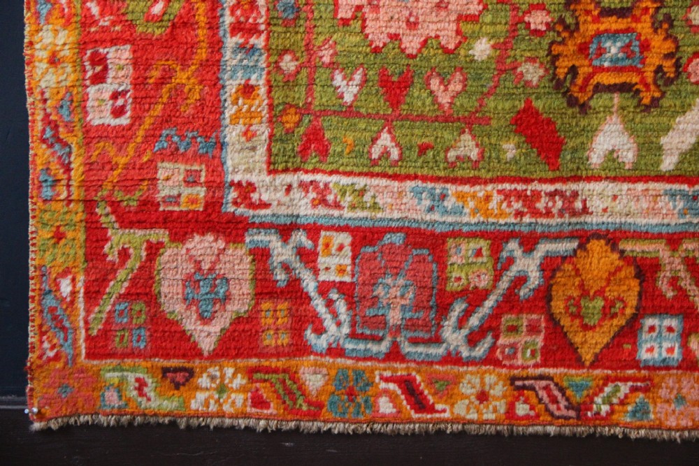An antique hand-knotted Oushak wool rug featuring an olive green field with soft red, pink, and cream floral medallions surrounded by a terracotta patterned border. View VII