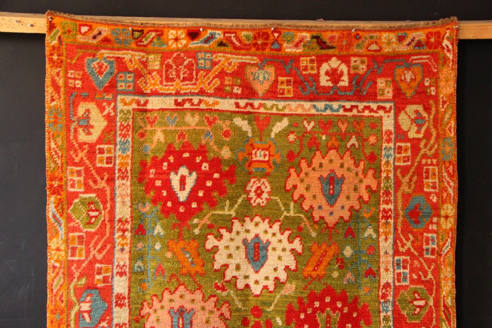 An antique hand-knotted Oushak wool rug featuring an olive green field with soft red, pink, and cream floral medallions surrounded by a terracotta patterned border. View X