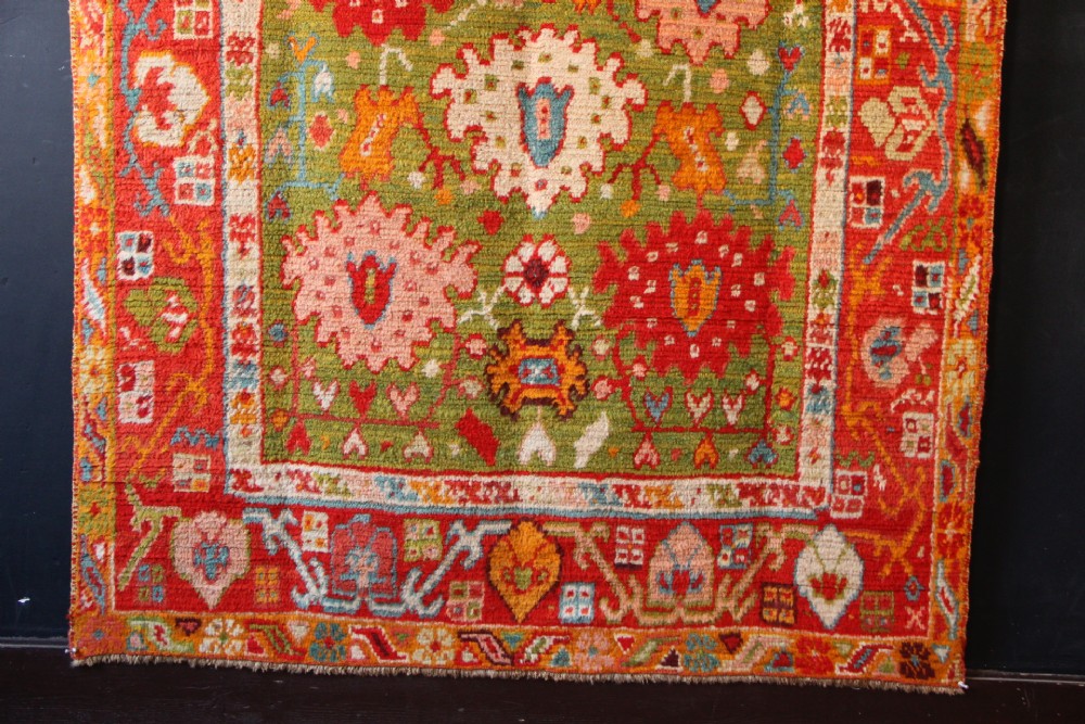 An antique hand-knotted Oushak wool rug featuring an olive green field with soft red, pink, and cream floral medallions surrounded by a terracotta patterned border. View XI