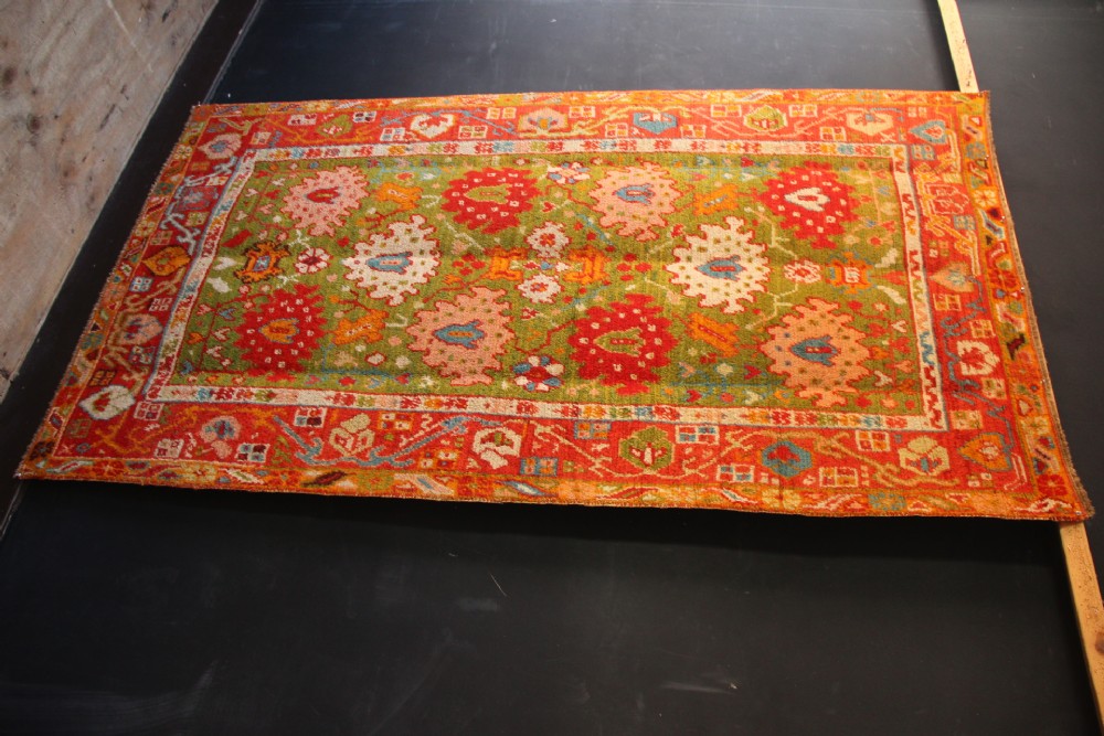 An antique hand-knotted Oushak wool rug featuring an olive green field with soft red, pink, and cream floral medallions surrounded by a terracotta patterned border. View XII