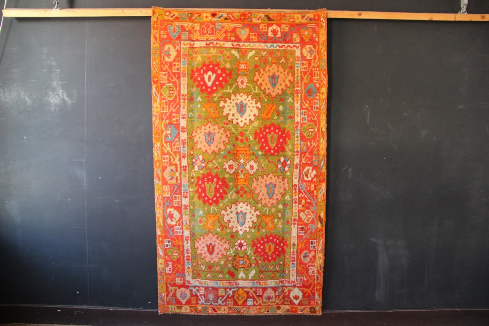 An antique hand-knotted Oushak wool rug featuring an olive green field with soft red, pink, and cream floral medallions surrounded by a terracotta patterned border. View XIII