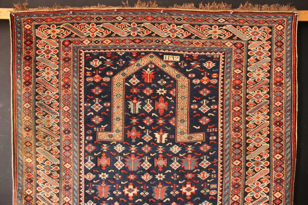 An antique Caucasian Kuba wool prayer rug featuring a dark navy field filled with small geometric motifs beneath a stepped arch border. View II