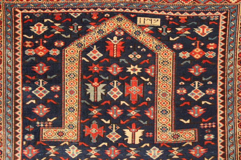 An antique Caucasian Kuba wool prayer rug featuring a dark navy field filled with small geometric motifs beneath a stepped arch border. View III