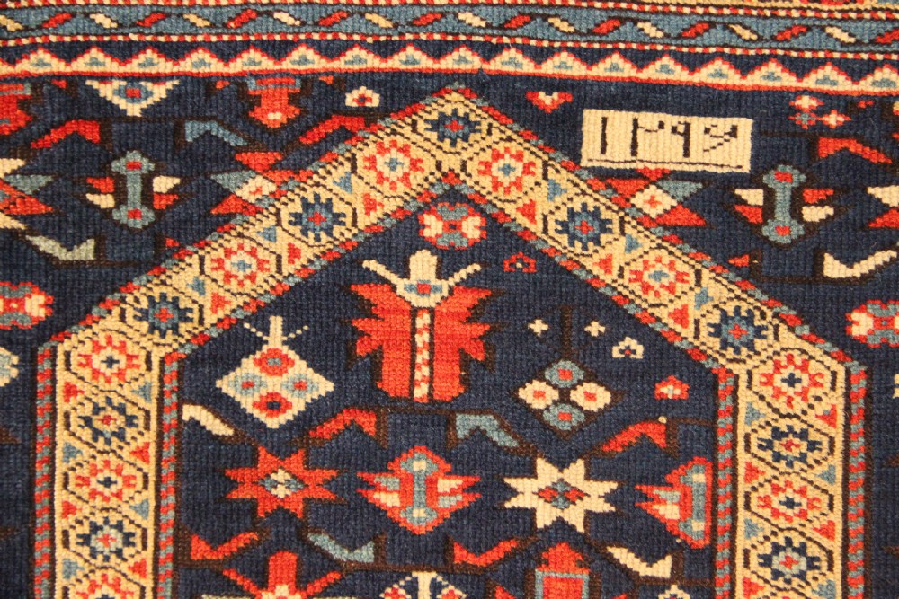 An antique Caucasian Kuba wool prayer rug featuring a dark navy field filled with small geometric motifs beneath a stepped arch border. View IV
