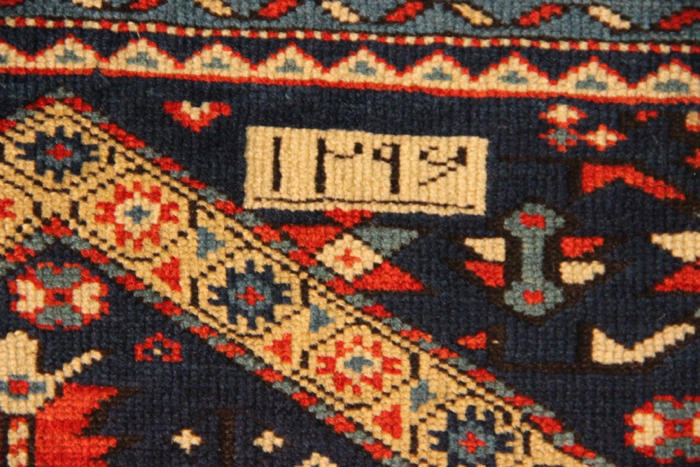 An antique Caucasian Kuba wool prayer rug featuring a dark navy field filled with small geometric motifs beneath a stepped arch border. View V