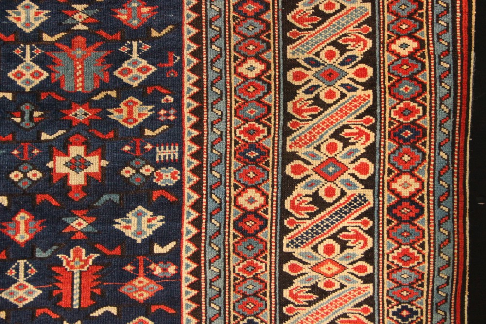 An antique Caucasian Kuba wool prayer rug featuring a dark navy field filled with small geometric motifs beneath a stepped arch border. View VI