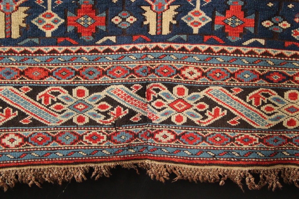 An antique Caucasian Kuba wool prayer rug featuring a dark navy field filled with small geometric motifs beneath a stepped arch border. View IX