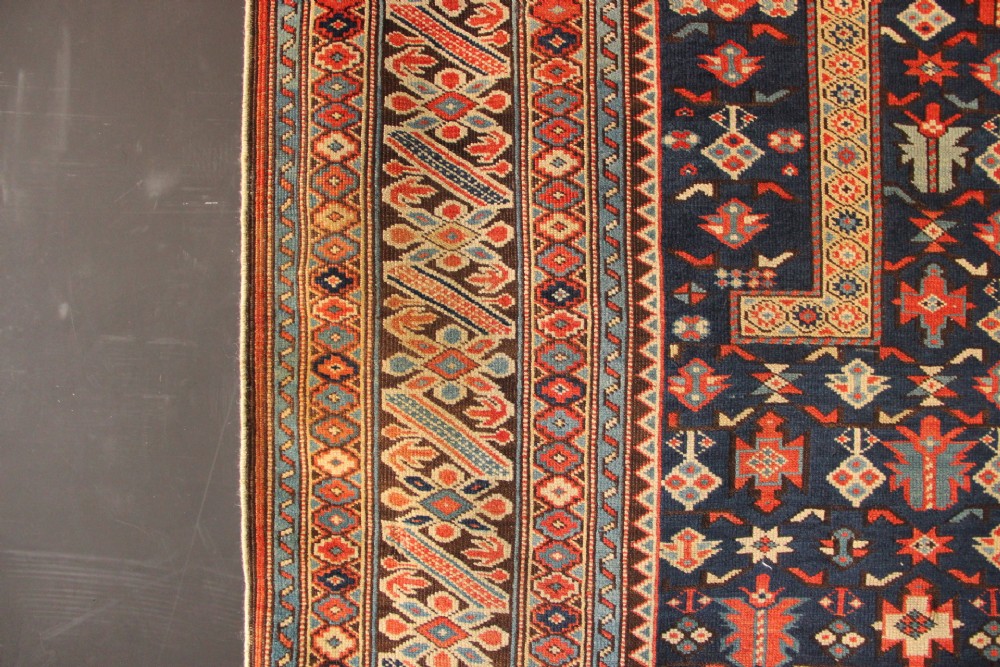 An antique Caucasian Kuba wool prayer rug featuring a dark navy field filled with small geometric motifs beneath a stepped arch border. View X