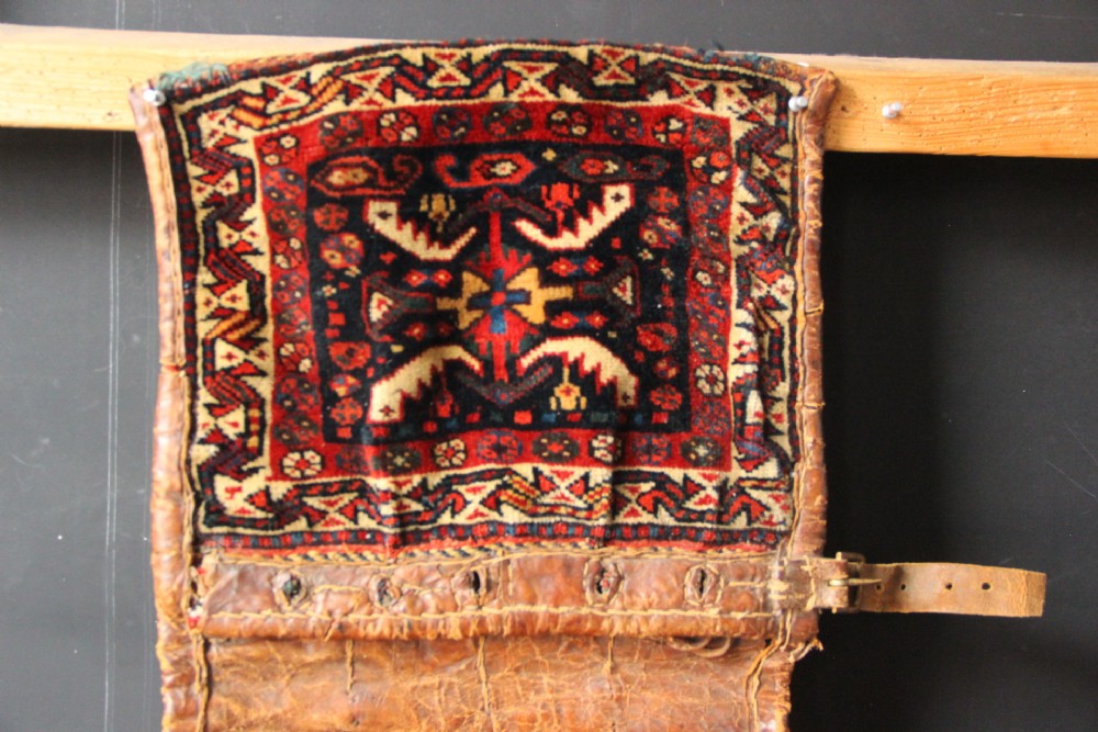 An antique miniature Khamseh tribal saddlebag featuring two hand-woven wool panels with deep red and navy geometric bird motifs joined by a leather centre section with straps. View II