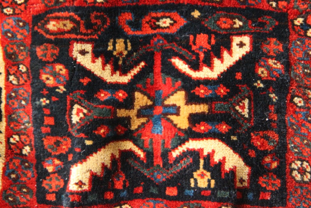 An antique miniature Khamseh tribal saddlebag featuring two hand-woven wool panels with deep red and navy geometric bird motifs joined by a leather centre section with straps. View IV