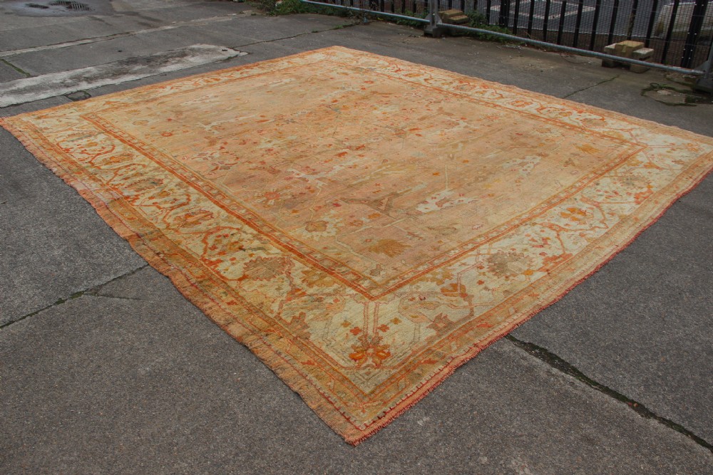 An oversized antique Turkish Oushak wool carpet featuring soft apricot, terracotta, and cream tones with traditional botanical borders and motifs.