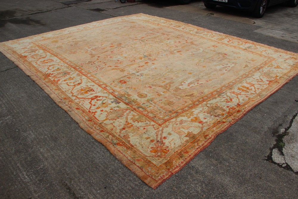 An oversized antique Turkish Oushak wool carpet featuring soft apricot, terracotta, and cream tones with traditional botanical borders and motifs. View V