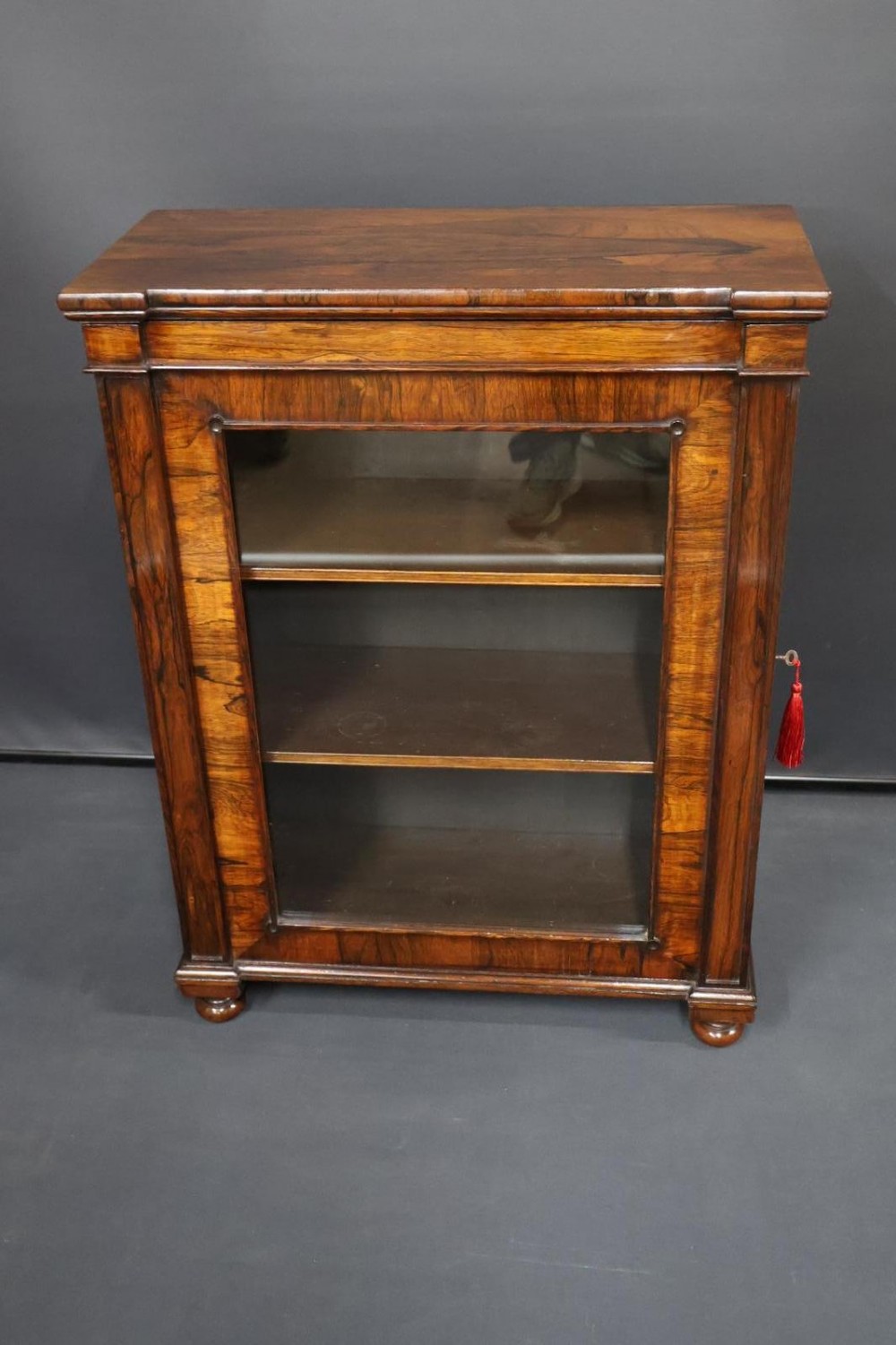 A Regency dark rosewood pier cabinet featuring a single glazed door revealing internal shelves, set on turned bun feet. View II