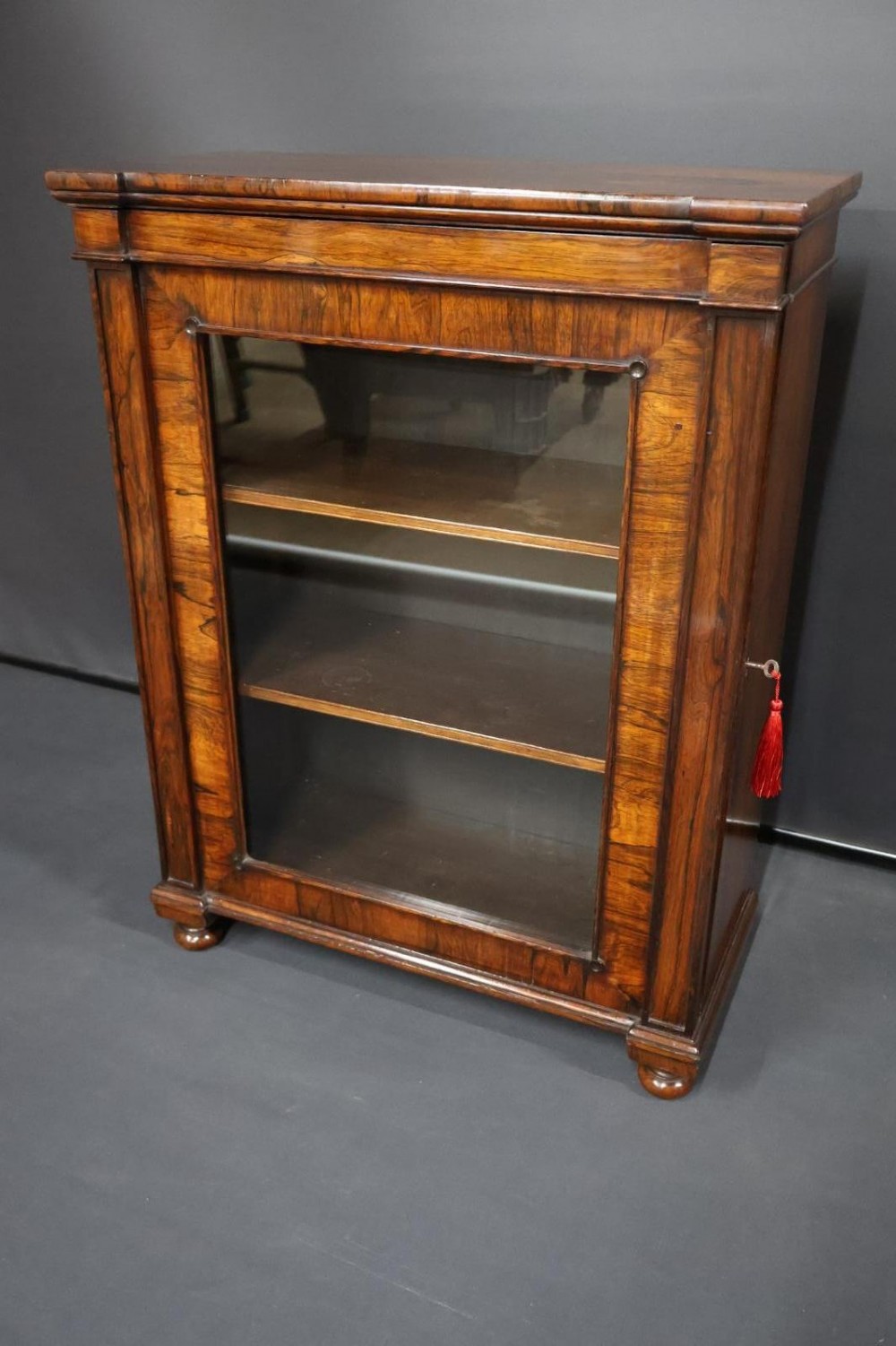 A Regency dark rosewood pier cabinet featuring a single glazed door revealing internal shelves, set on turned bun feet. View III