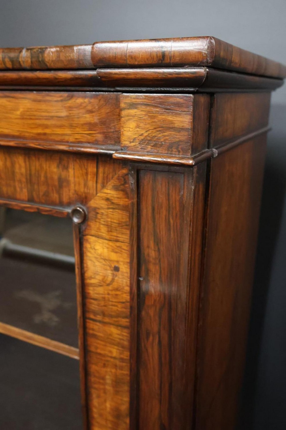 A Regency dark rosewood pier cabinet featuring a single glazed door revealing internal shelves, set on turned bun feet. View IV