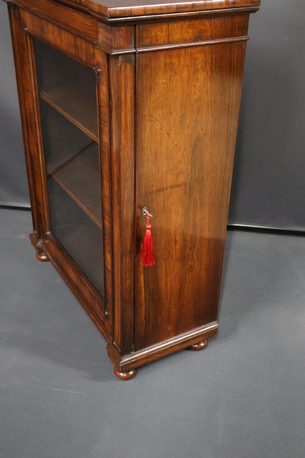 A Regency dark rosewood pier cabinet featuring a single glazed door revealing internal shelves, set on turned bun feet. View X