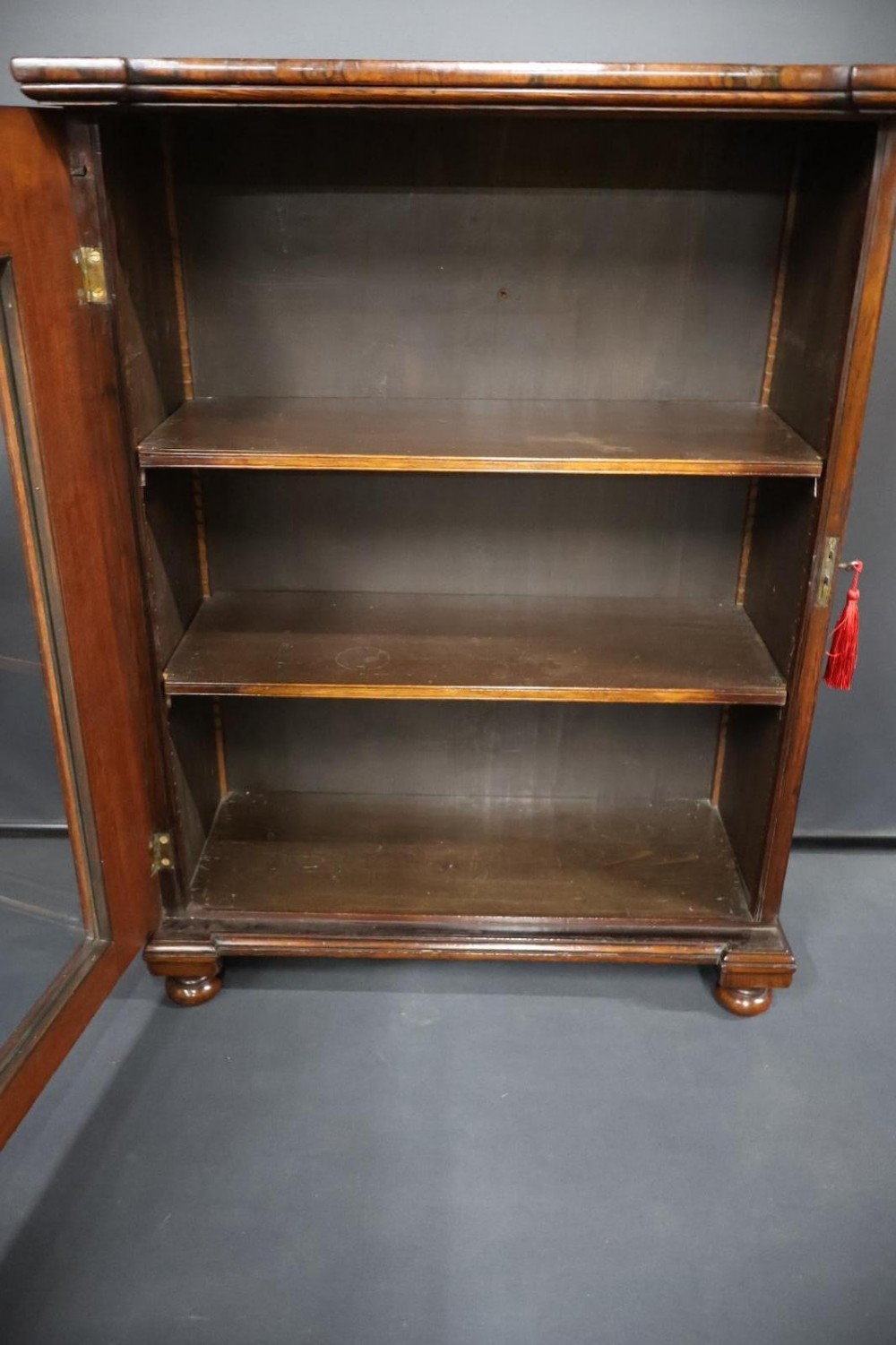 A Regency dark rosewood pier cabinet featuring a single glazed door revealing internal shelves, set on turned bun feet. View XIII