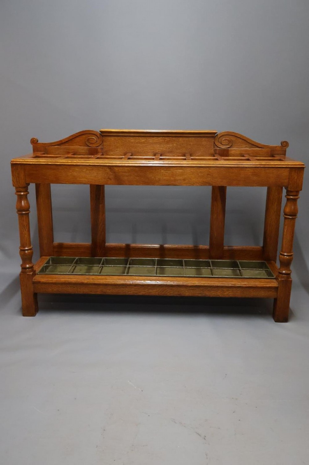 A large Victorian carved oak umbrella and stick stand featuring turned front supports, multiple upper divisions, and a metal drip tray at the base.