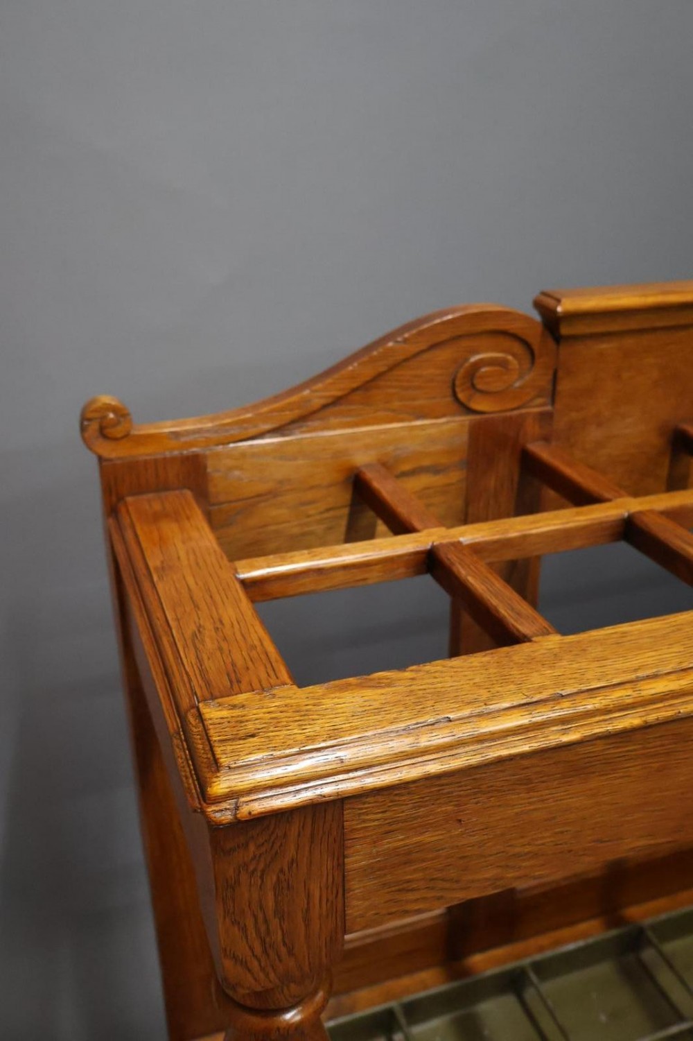 A large Victorian carved oak umbrella and stick stand featuring turned front supports, multiple upper divisions, and a metal drip tray at the base. View V