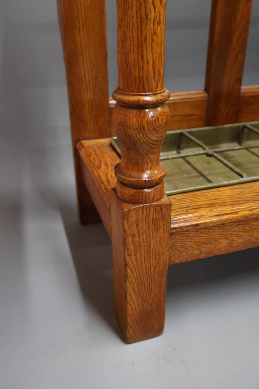 A large Victorian carved oak umbrella and stick stand featuring turned front supports, multiple upper divisions, and a metal drip tray at the base. View VI