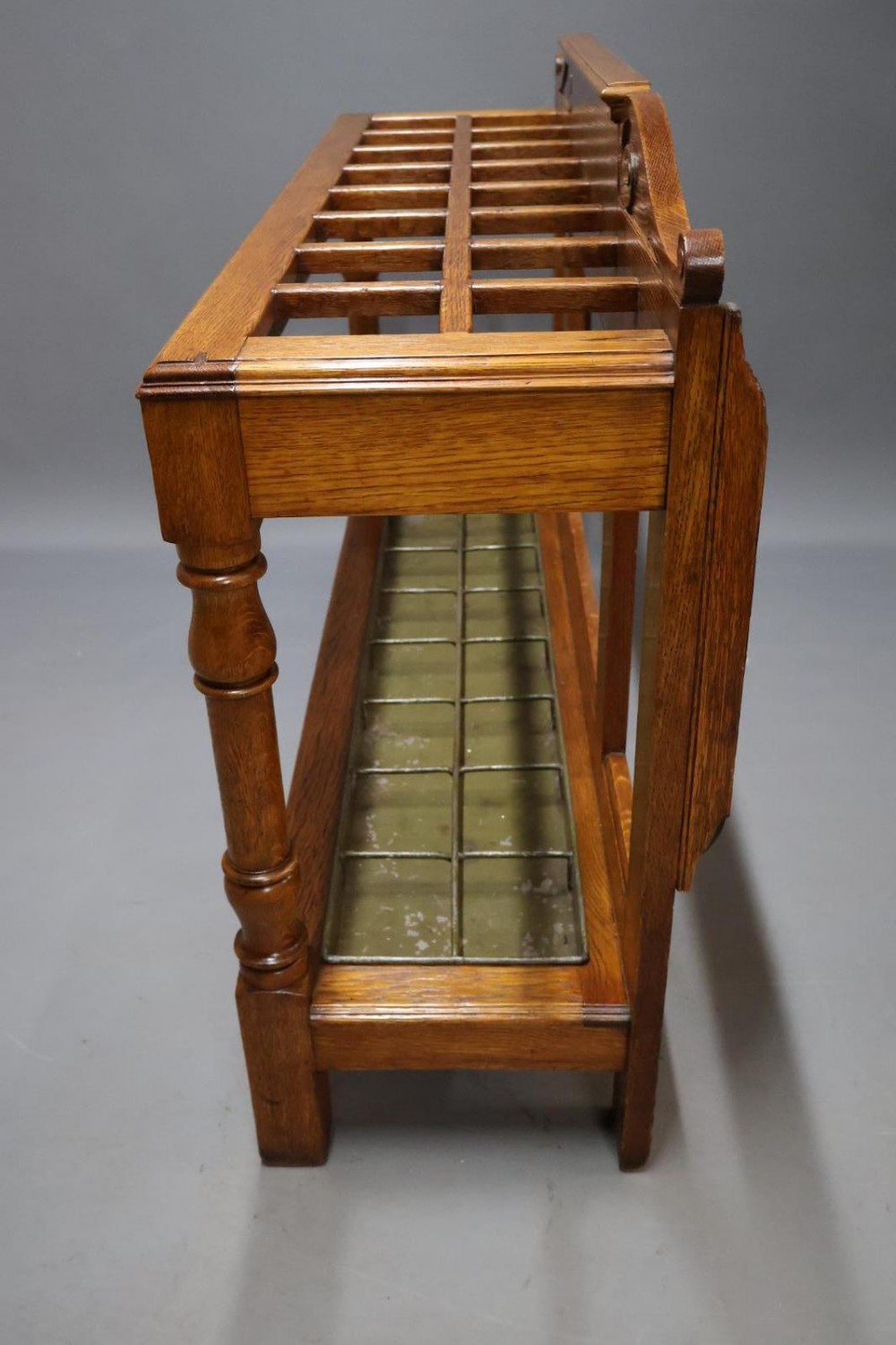 A large Victorian carved oak umbrella and stick stand featuring turned front supports, multiple upper divisions, and a metal drip tray at the base. View IX