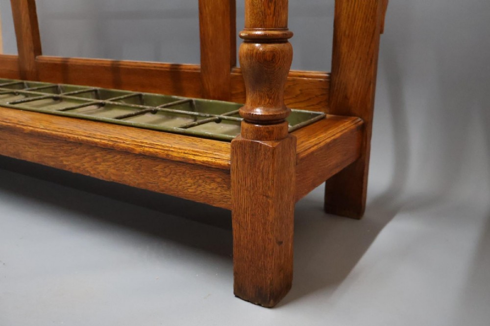 A large Victorian carved oak umbrella and stick stand featuring turned front supports, multiple upper divisions, and a metal drip tray at the base. View X