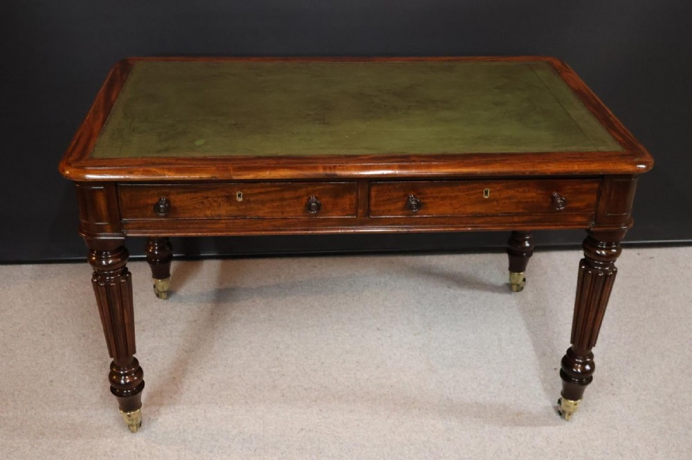 An early nineteenth-century mahogany writing table featuring an inset green leather writing surface, two frieze drawers, and reeded turned legs on brass castors.