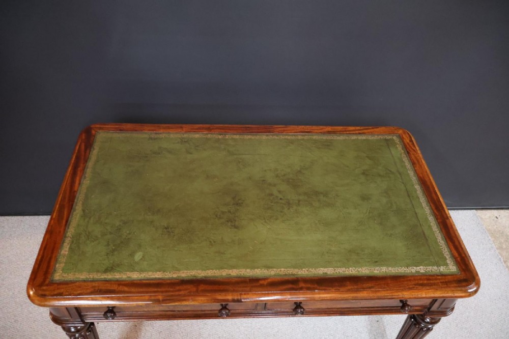 An early nineteenth-century mahogany writing table featuring an inset green leather writing surface, two frieze drawers, and reeded turned legs on brass castors. View II