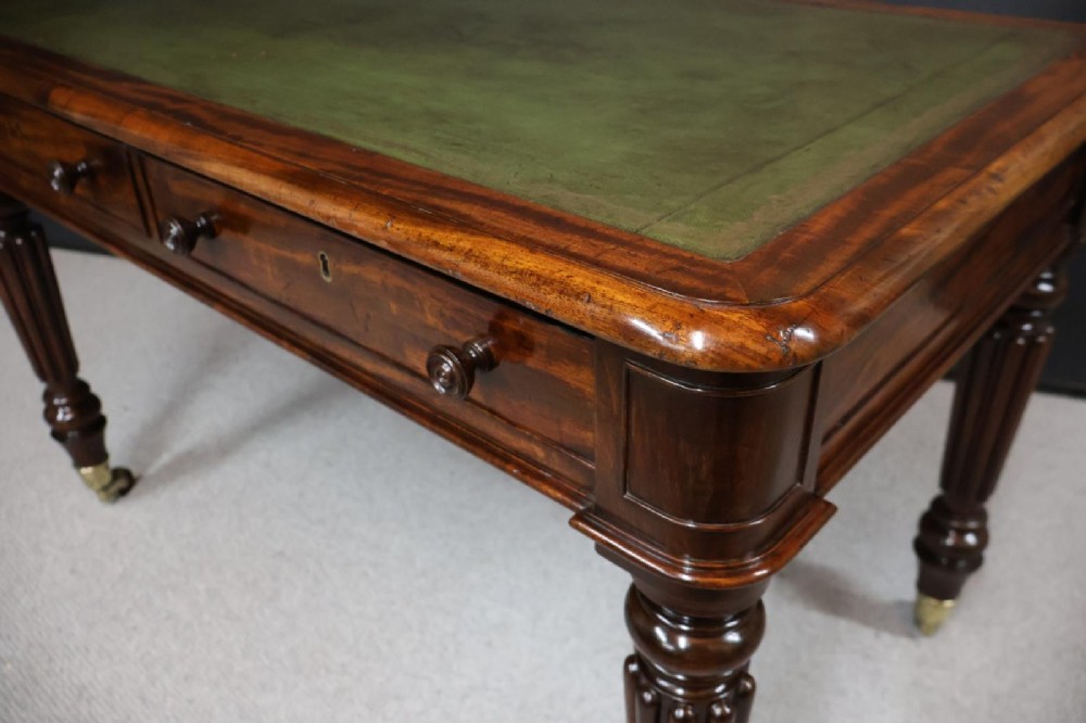 An early nineteenth-century mahogany writing table featuring an inset green leather writing surface, two frieze drawers, and reeded turned legs on brass castors. View IV