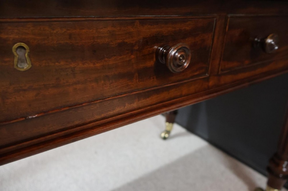An early nineteenth-century mahogany writing table featuring an inset green leather writing surface, two frieze drawers, and reeded turned legs on brass castors. View VII