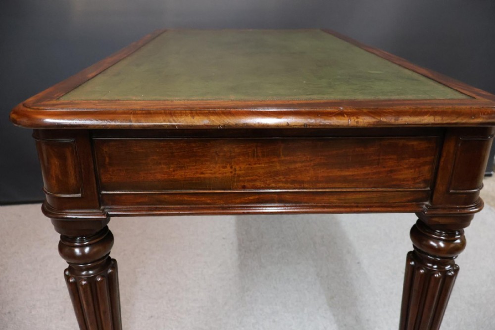 An early nineteenth-century mahogany writing table featuring an inset green leather writing surface, two frieze drawers, and reeded turned legs on brass castors. View X