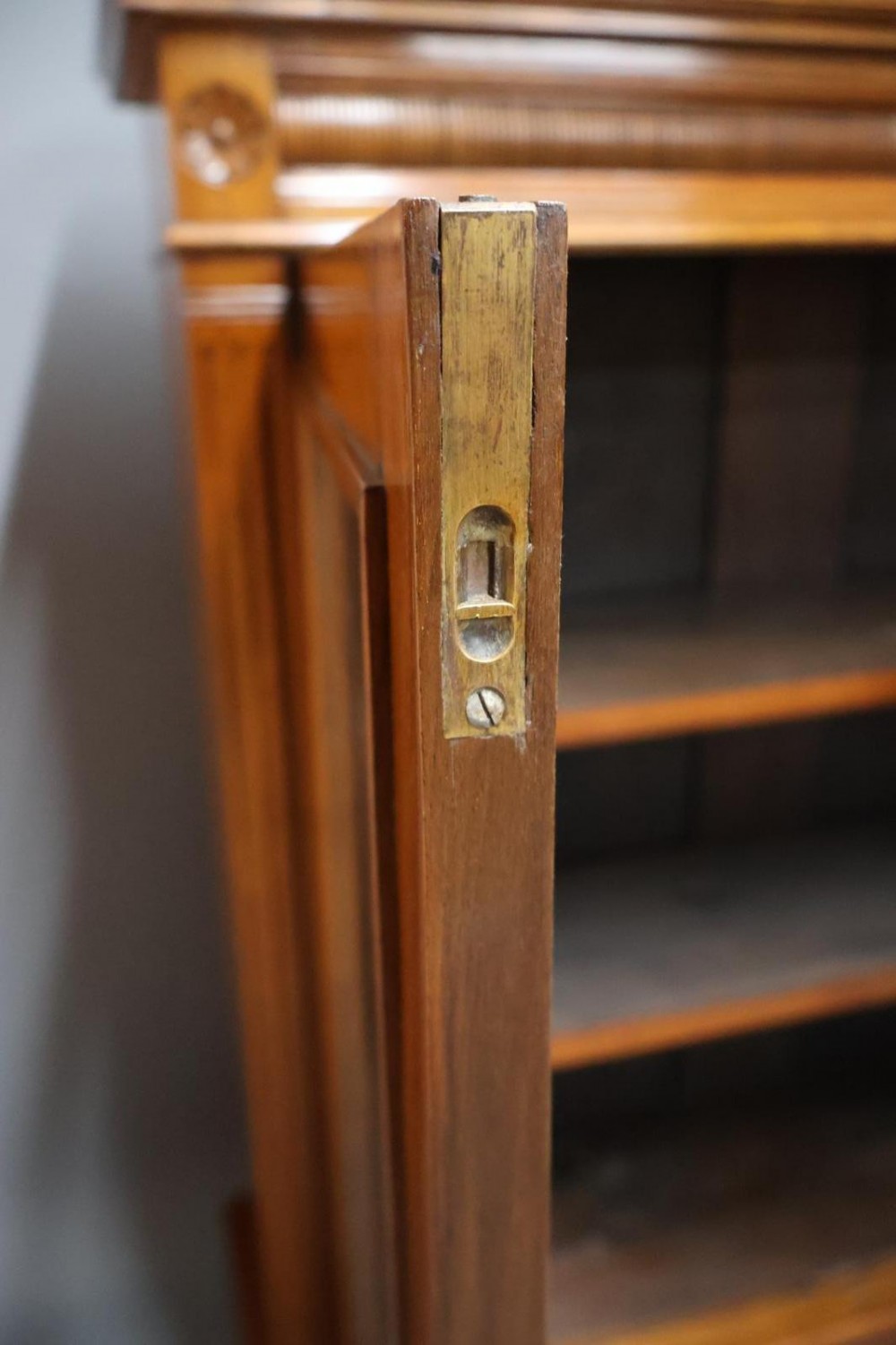 An Edwardian low walnut bookcase featuring two glass-fronted doors, reeded frieze detailing, fluted pilasters, and shelves filled with leather-bound books. View V