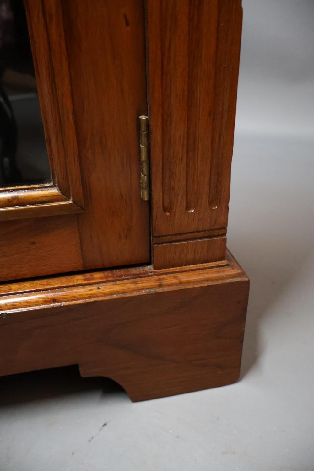 An Edwardian low walnut bookcase featuring two glass-fronted doors, reeded frieze detailing, fluted pilasters, and shelves filled with leather-bound books. View VIII