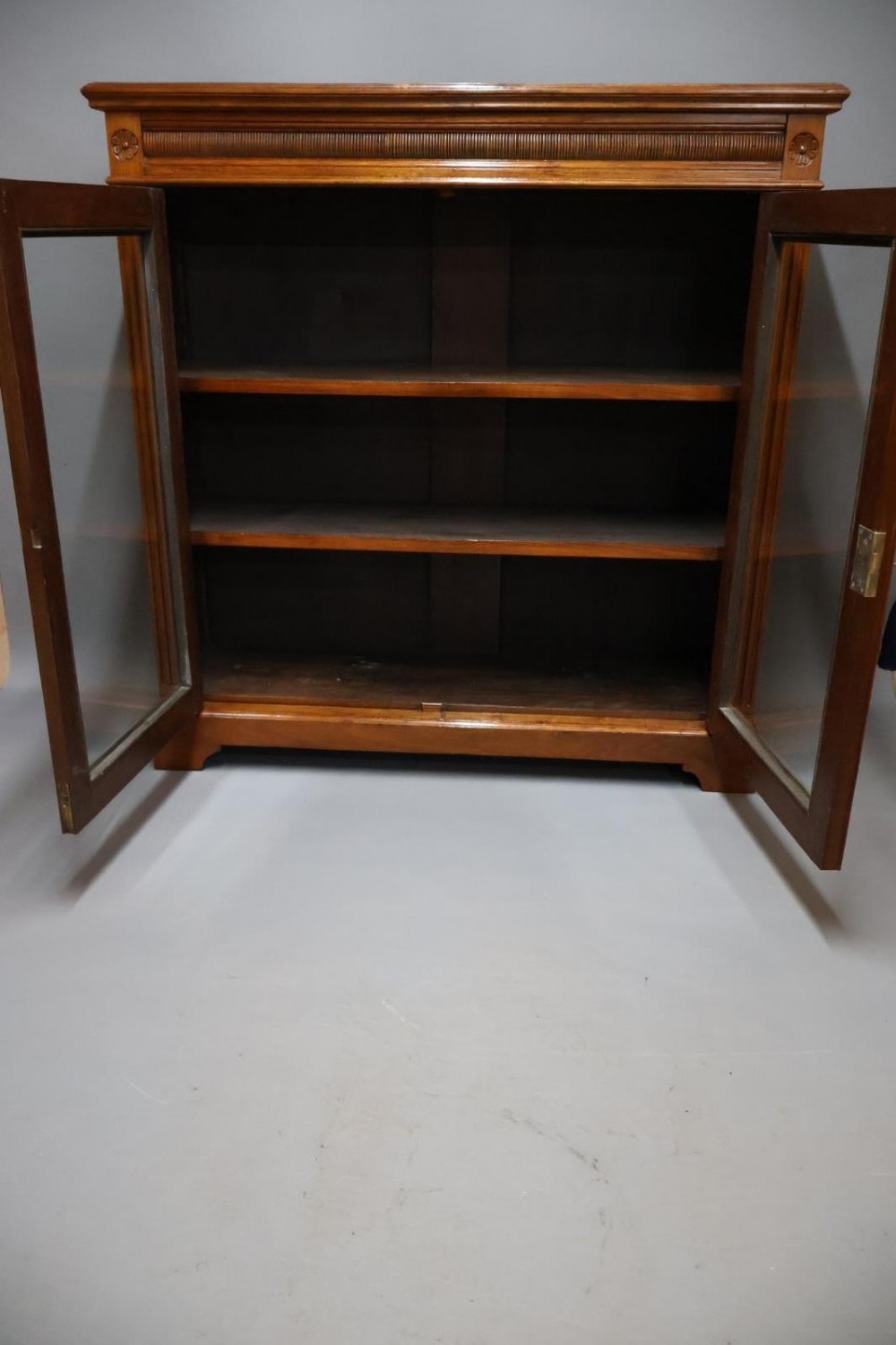 An Edwardian low walnut bookcase featuring two glass-fronted doors, reeded frieze detailing, fluted pilasters, and shelves filled with leather-bound books. View XI