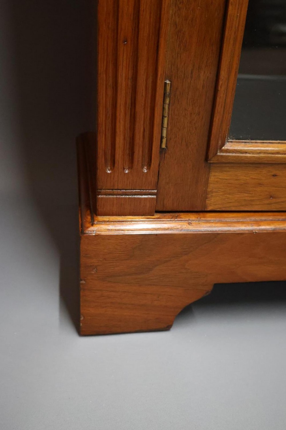 An Edwardian low walnut bookcase featuring two glass-fronted doors, reeded frieze detailing, fluted pilasters, and shelves filled with leather-bound books. View XII
