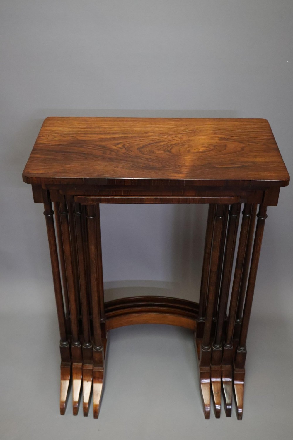 A set of four nested Regency rosewood tables featuring rectangular tops, slender turned spindle legs, and curved lower stretchers.