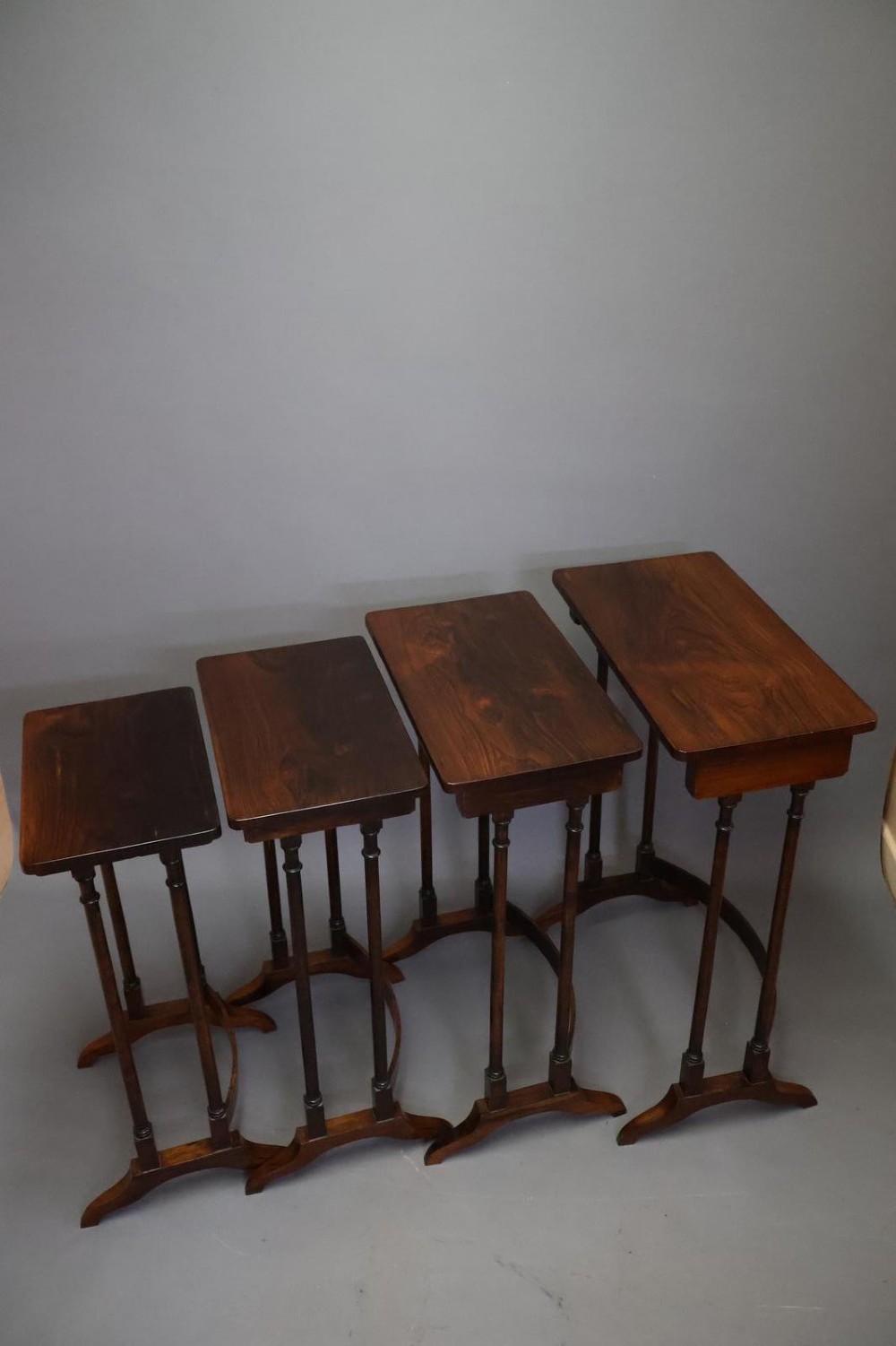 A set of four nested Regency rosewood tables featuring rectangular tops, slender turned spindle legs, and curved lower stretchers. View V