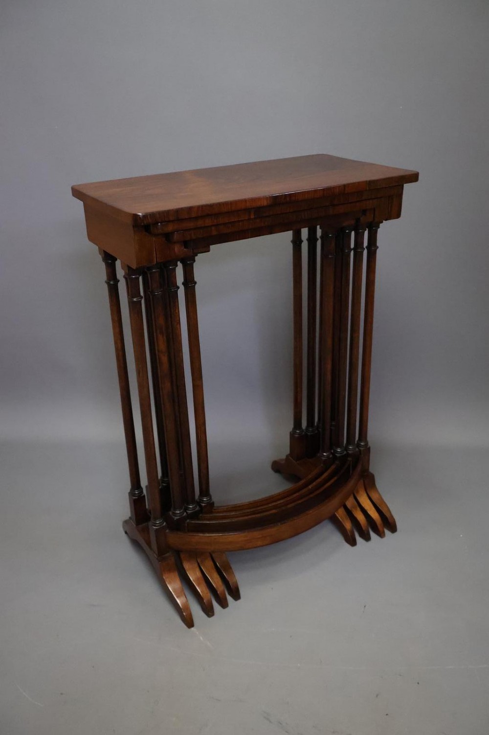 A set of four nested Regency rosewood tables featuring rectangular tops, slender turned spindle legs, and curved lower stretchers. View X