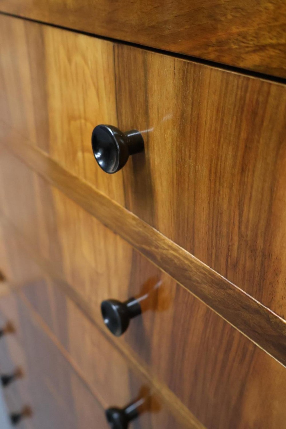 An Art Deco walnut tallboy chest of drawers featuring eight vertically stacked drawers with figured wood grain, round black handles, and an ebonised base. View II