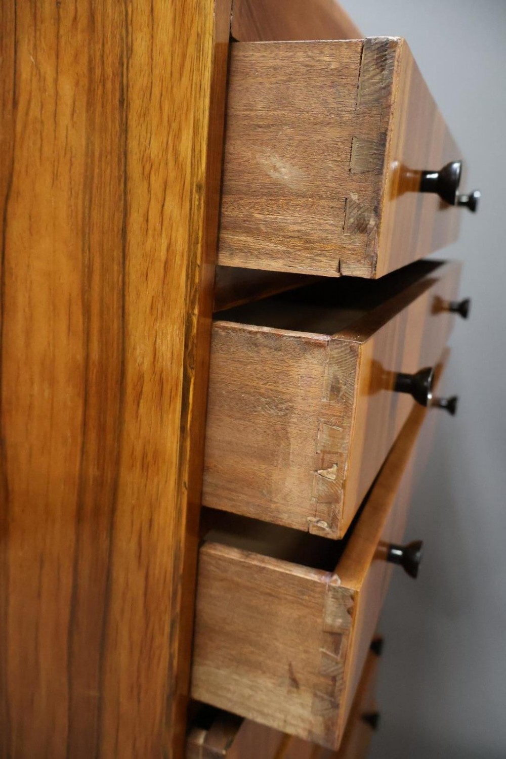 An Art Deco walnut tallboy chest of drawers featuring eight vertically stacked drawers with figured wood grain, round black handles, and an ebonised base. View VIII