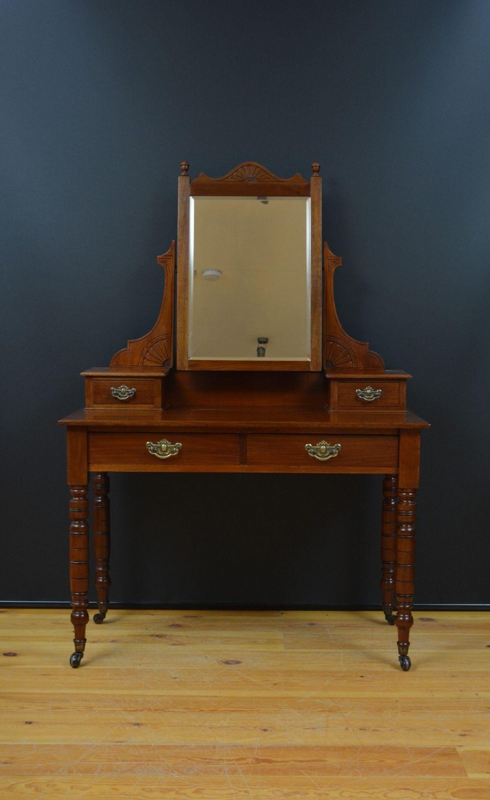 An Edwardian mahogany dressing table featuring a central rectangular mirror flanked by small jewellery drawers, resting on turned legs with brass casters.