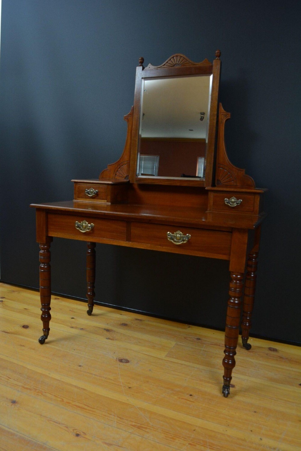 An Edwardian mahogany dressing table featuring a central rectangular mirror flanked by small jewellery drawers, resting on turned legs with brass casters. View II