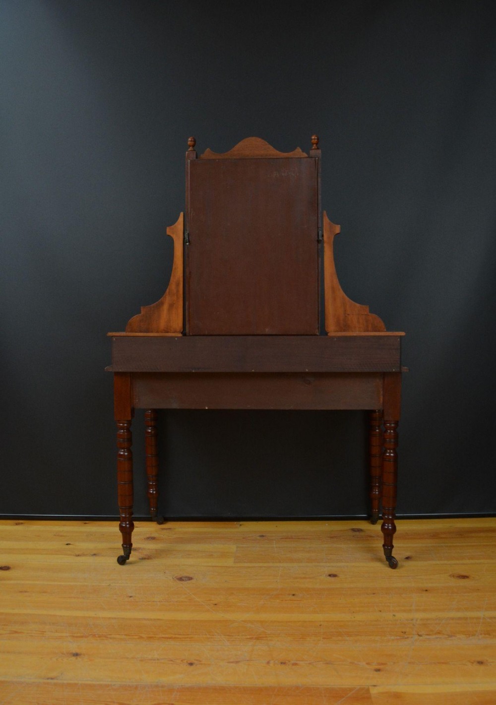 An Edwardian mahogany dressing table featuring a central rectangular mirror flanked by small jewellery drawers, resting on turned legs with brass casters. View V