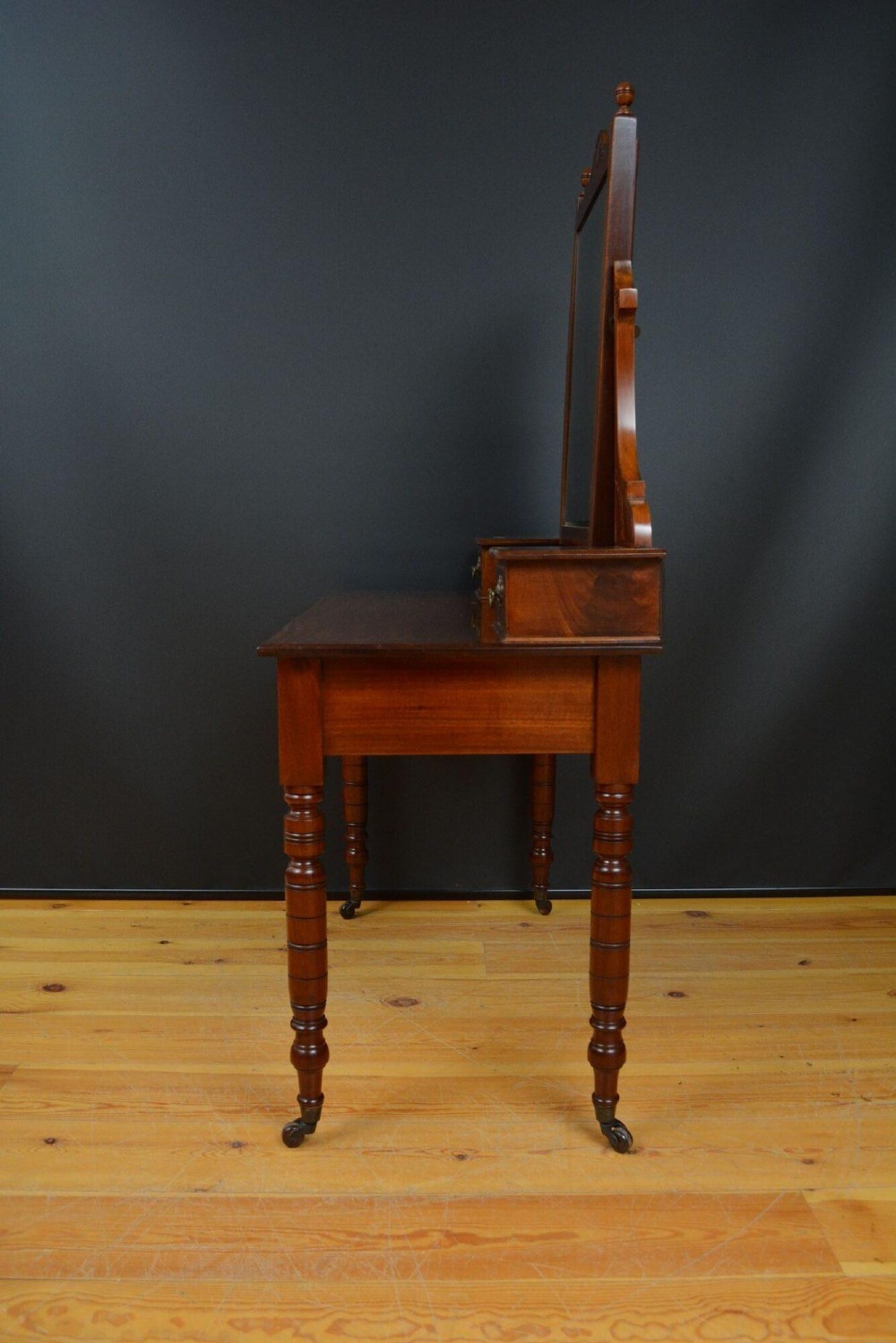 An Edwardian mahogany dressing table featuring a central rectangular mirror flanked by small jewellery drawers, resting on turned legs with brass casters. View VIII