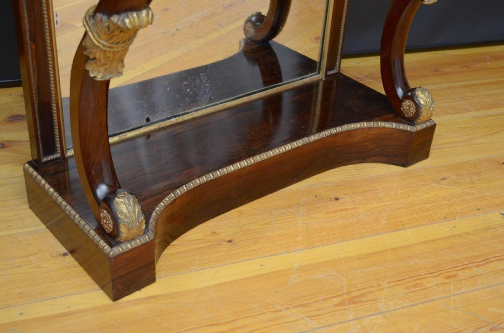 A Regency rosewood console table featuring an upper shelf tier, mirror-backed panels, and gilt carved scroll legs. View IV