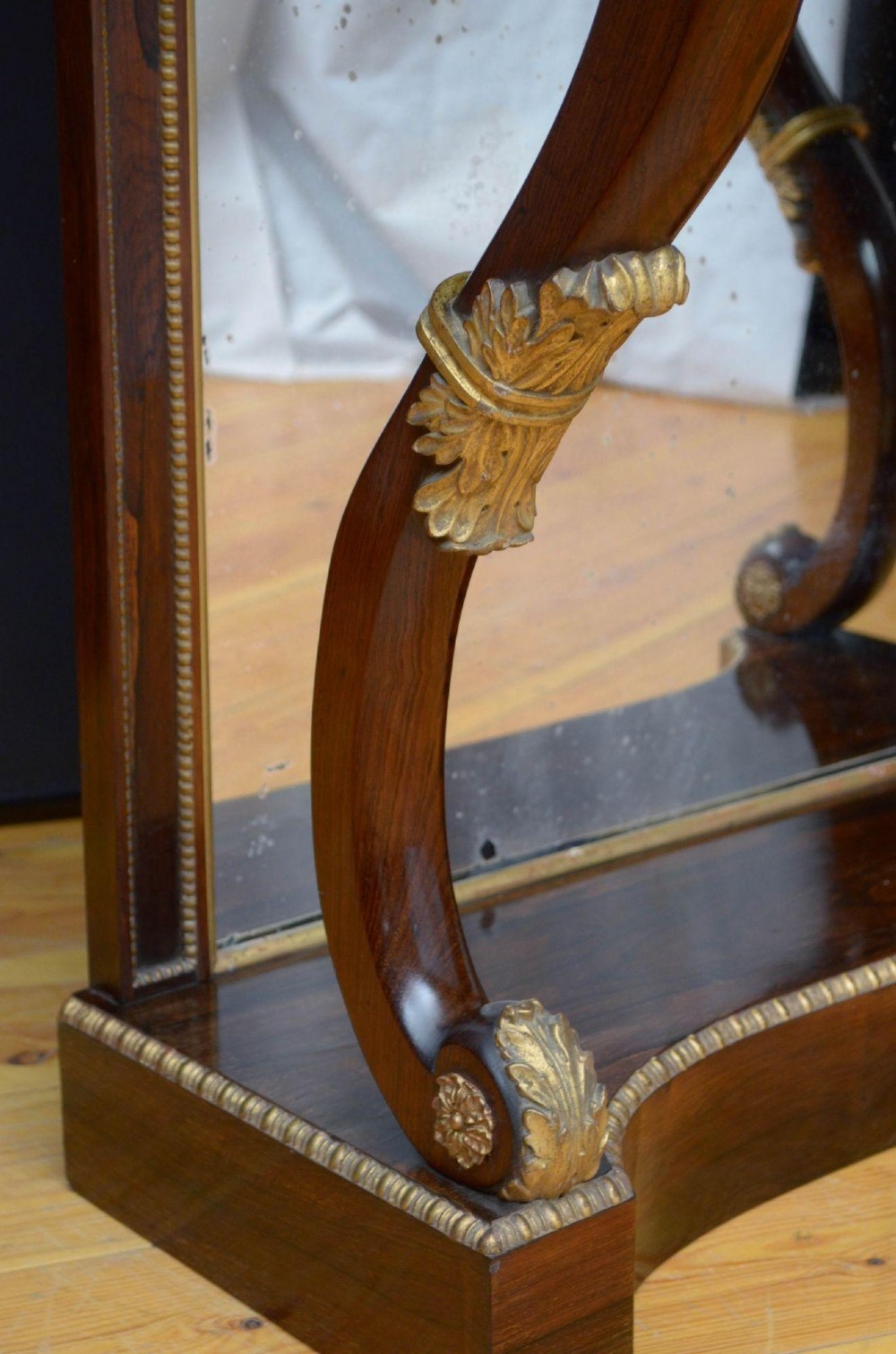 A Regency rosewood console table featuring an upper shelf tier, mirror-backed panels, and gilt carved scroll legs. View V