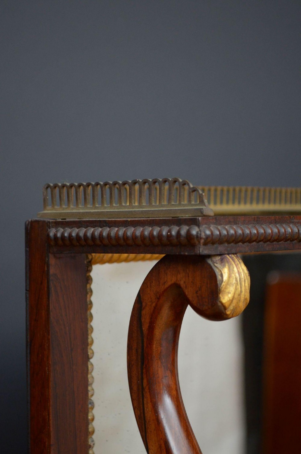 A Regency rosewood console table featuring an upper shelf tier, mirror-backed panels, and gilt carved scroll legs. View VI