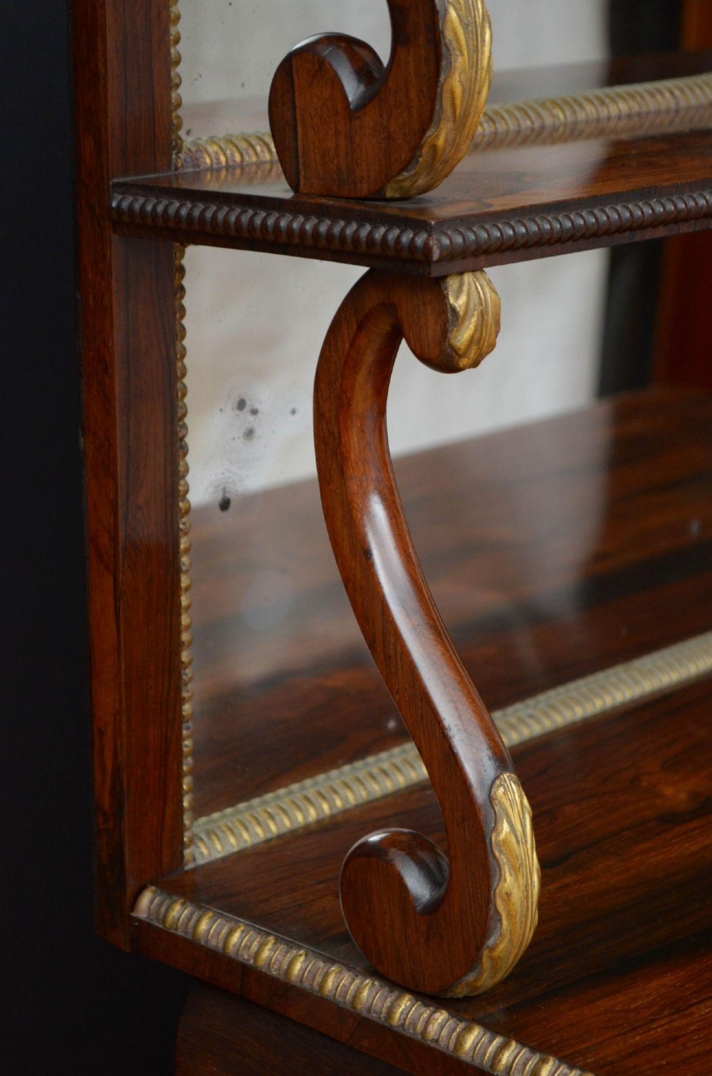 A Regency rosewood console table featuring an upper shelf tier, mirror-backed panels, and gilt carved scroll legs. View VII