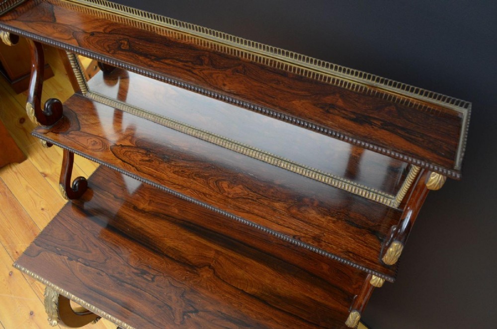 A Regency rosewood console table featuring an upper shelf tier, mirror-backed panels, and gilt carved scroll legs. View VIII