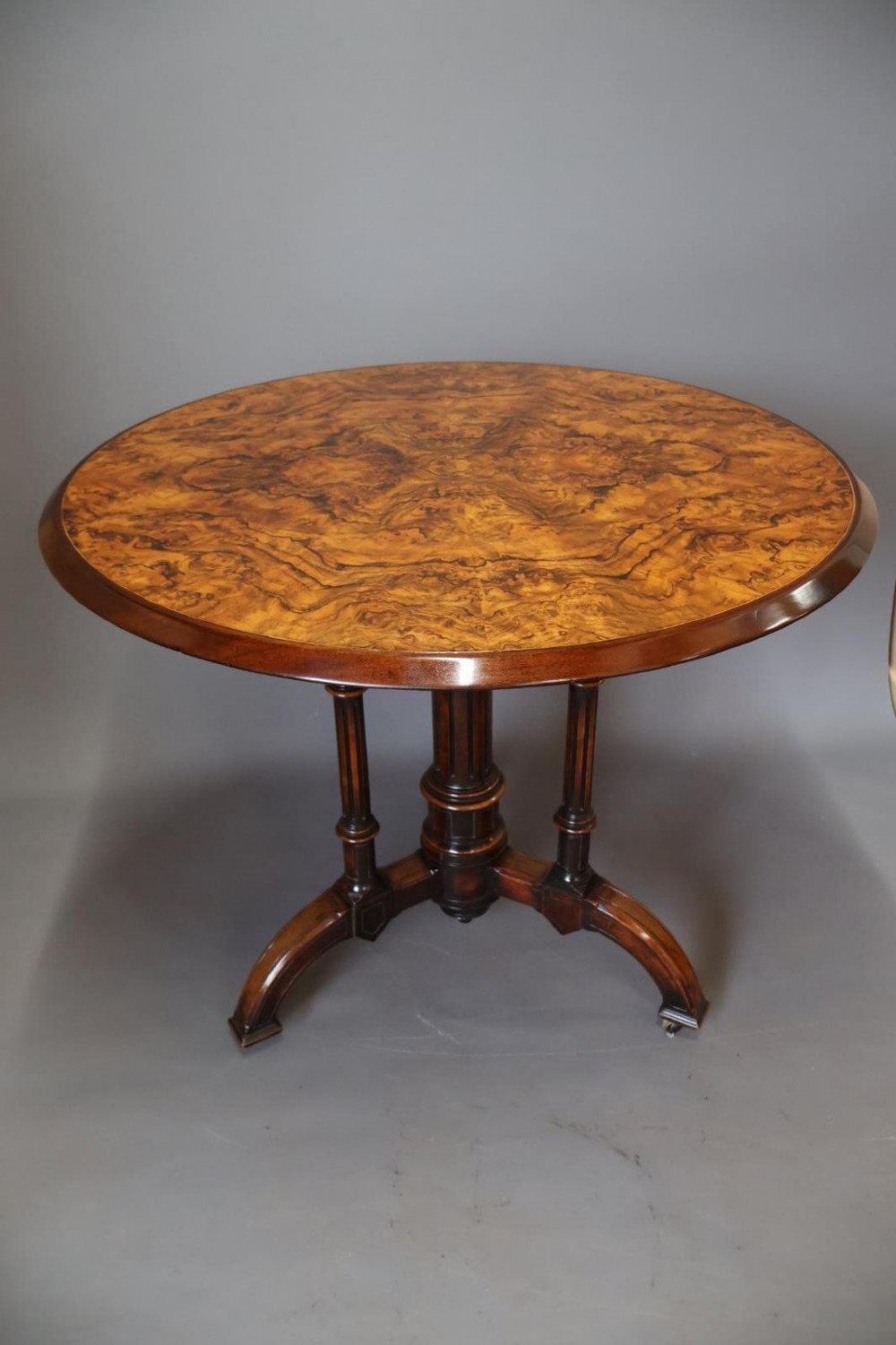 A circular burr walnut centre table featuring a figured top, turned central pedestal, four outer colonnettes, and splayed legs on castors.